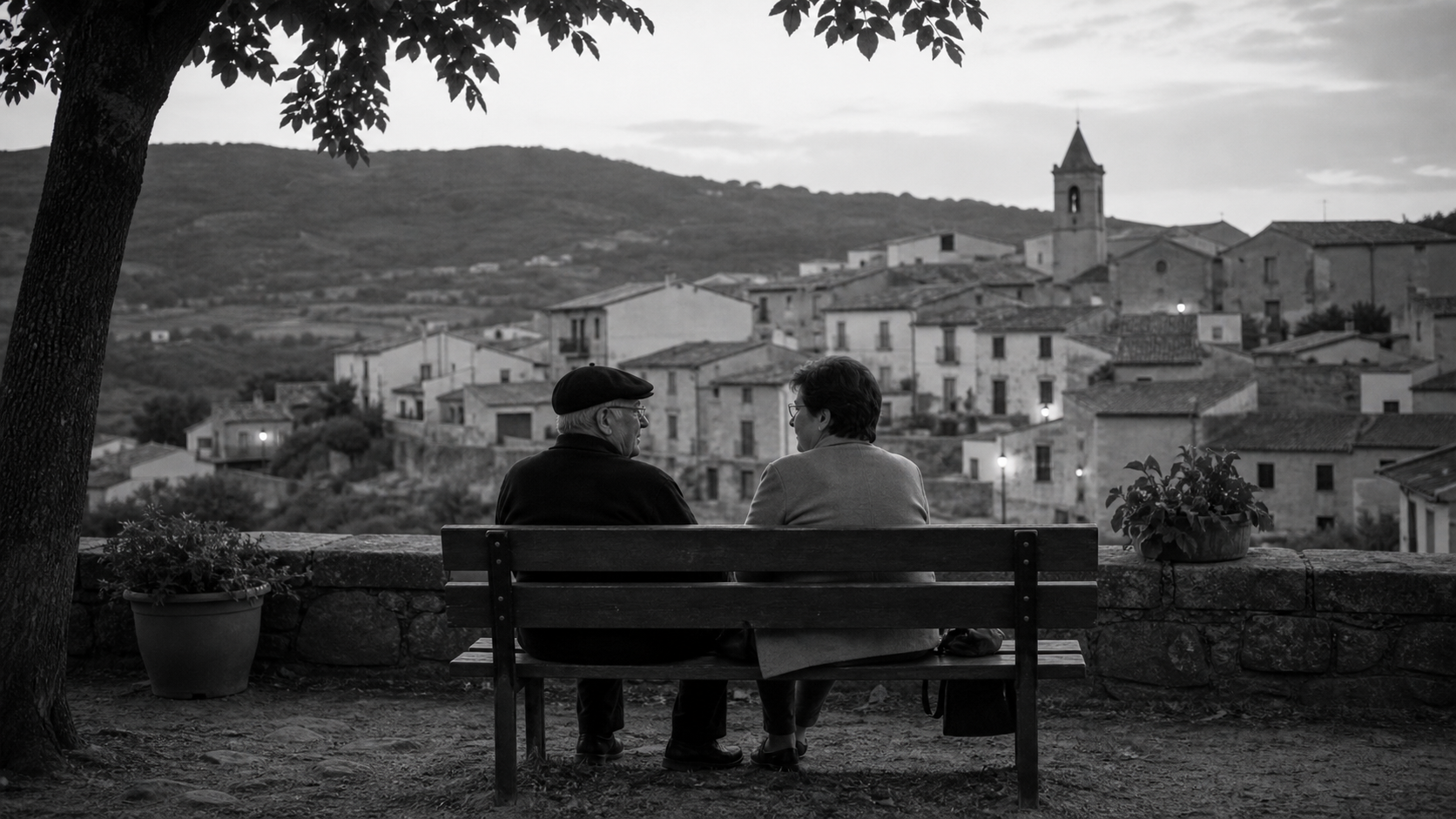 Dos personas conversando en un banco de pueblo.